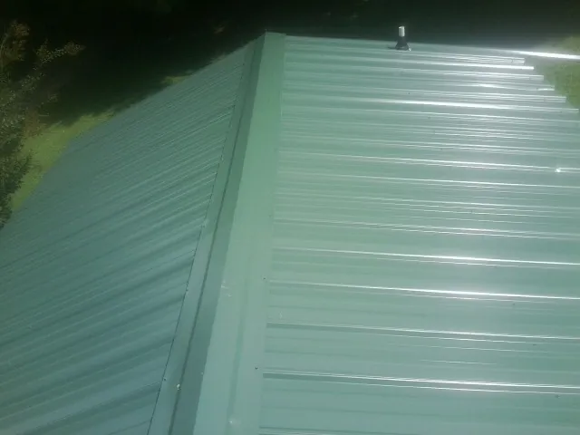 New green metal panels meeting at the ridge of a roof — Flat Roof Repair work by our crew in Sunnyside