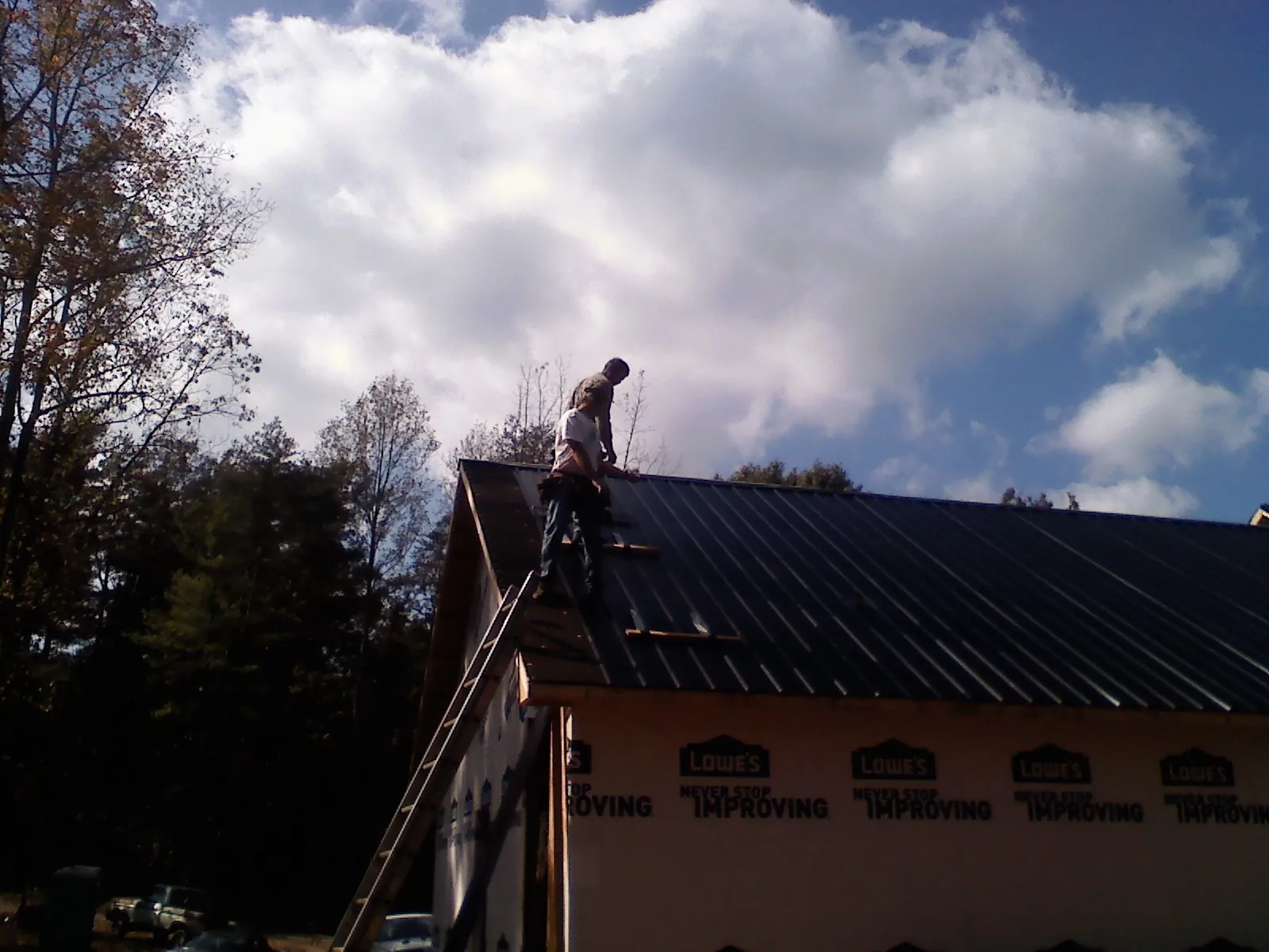 Roofer fastening dark metal panels high against a cloudy sky, from a Roof Inspection job in Sunnyside